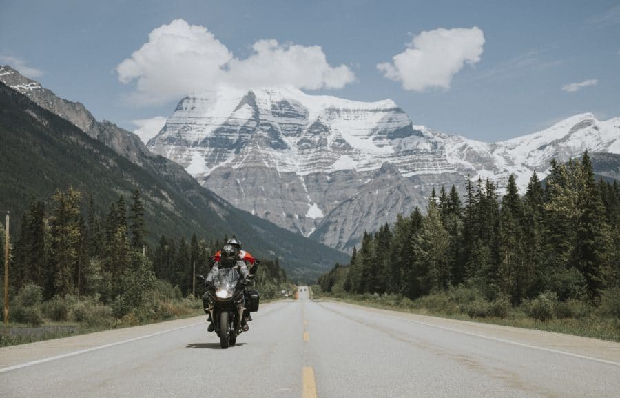 Motorcyclist riding down a two lane highway with Mount Robson rising up in the background.