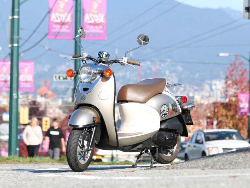 A parked single-seater scooter with a cityscape in the background