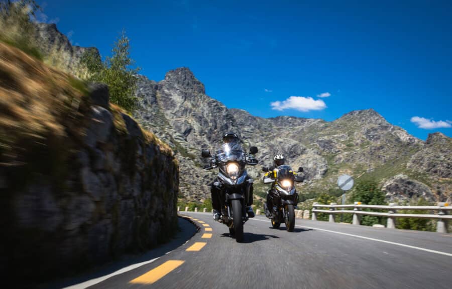 Two Suzuki V-Strom 650's wrapping around a corner with the road lines blurred and mountains in the background