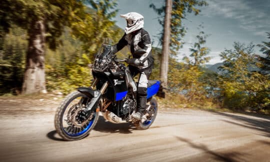 Yamaha Tenere 700 riding on a gravel road in the forest with the rider standing on the pegs.
