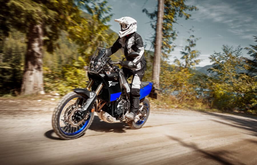 Yamaha Tenere 700 riding on a gravel road in the forest with the rider standing on the pegs.