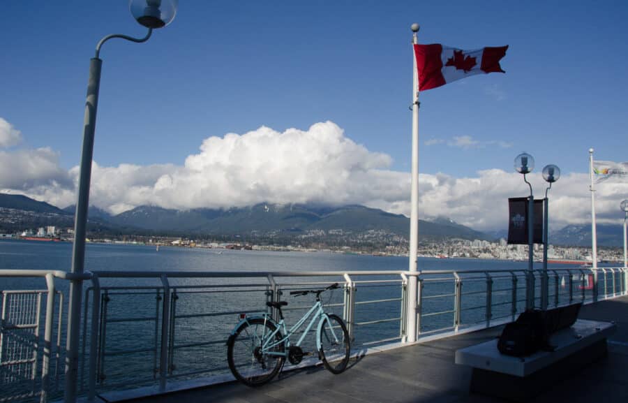 Bike lent against railing by a Canadian flag with mountains as a backdrop.