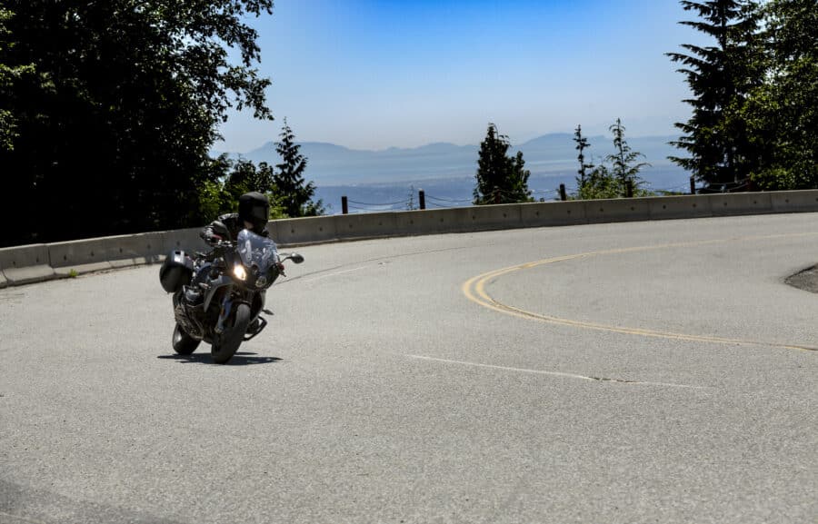 a motorcycle riding a curve with the mountains and ocean in the background.
