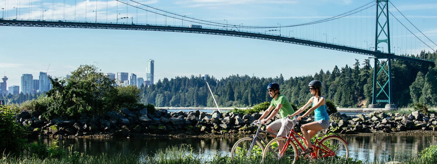 two cyclists riding seaside with the lions gate bridge in the background