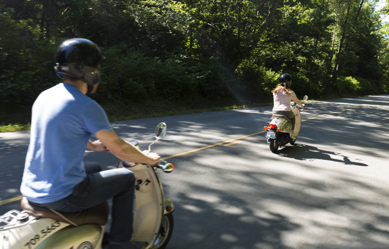 Two scooter riders on a forest road.