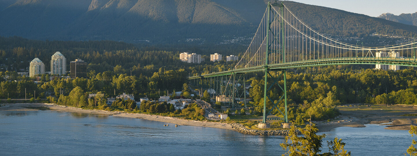 The Lions Gate Bridge over the Ocean with Mountains in the background.