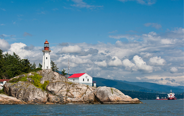 A lighthouse on a rocky outcropping with mountains in the background.