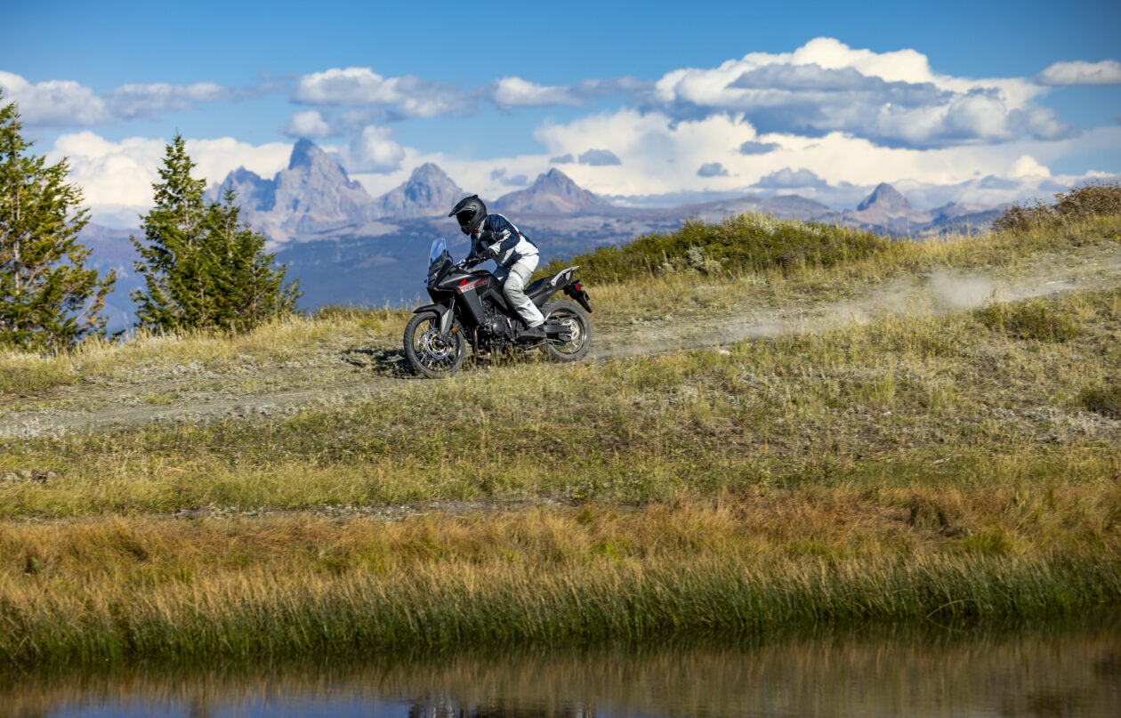 Riding a Honda Transalp on a dirt road with the mountains in the background.