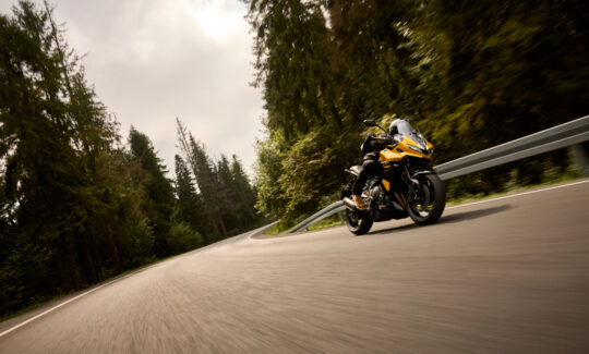 A rider going fast on a yellow Triumph Tigersport 800