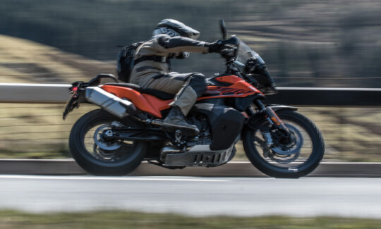 Motorcyclist rides orange motorcycle on highway.