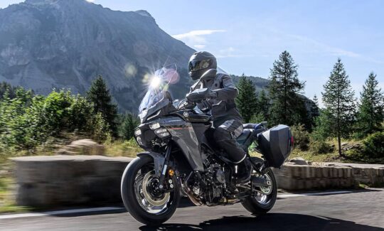 Motorcyclist on scenic mountain road in sunny weather.