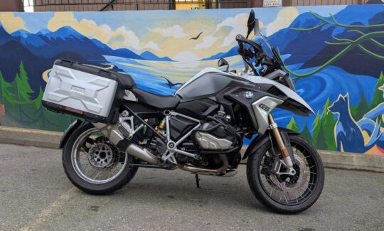 Motorcycle parked by colourful mural wall.