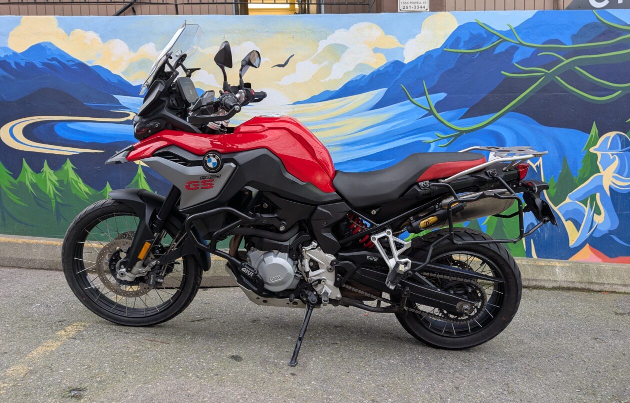 Red motorcycle parked by mountain mural wall.