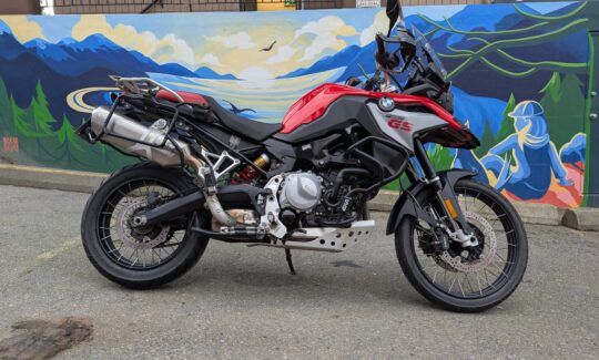 Red motorcycle parked by colourful mural wall.