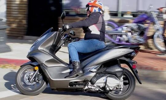 Person riding scooter wearing Union Jack helmet.